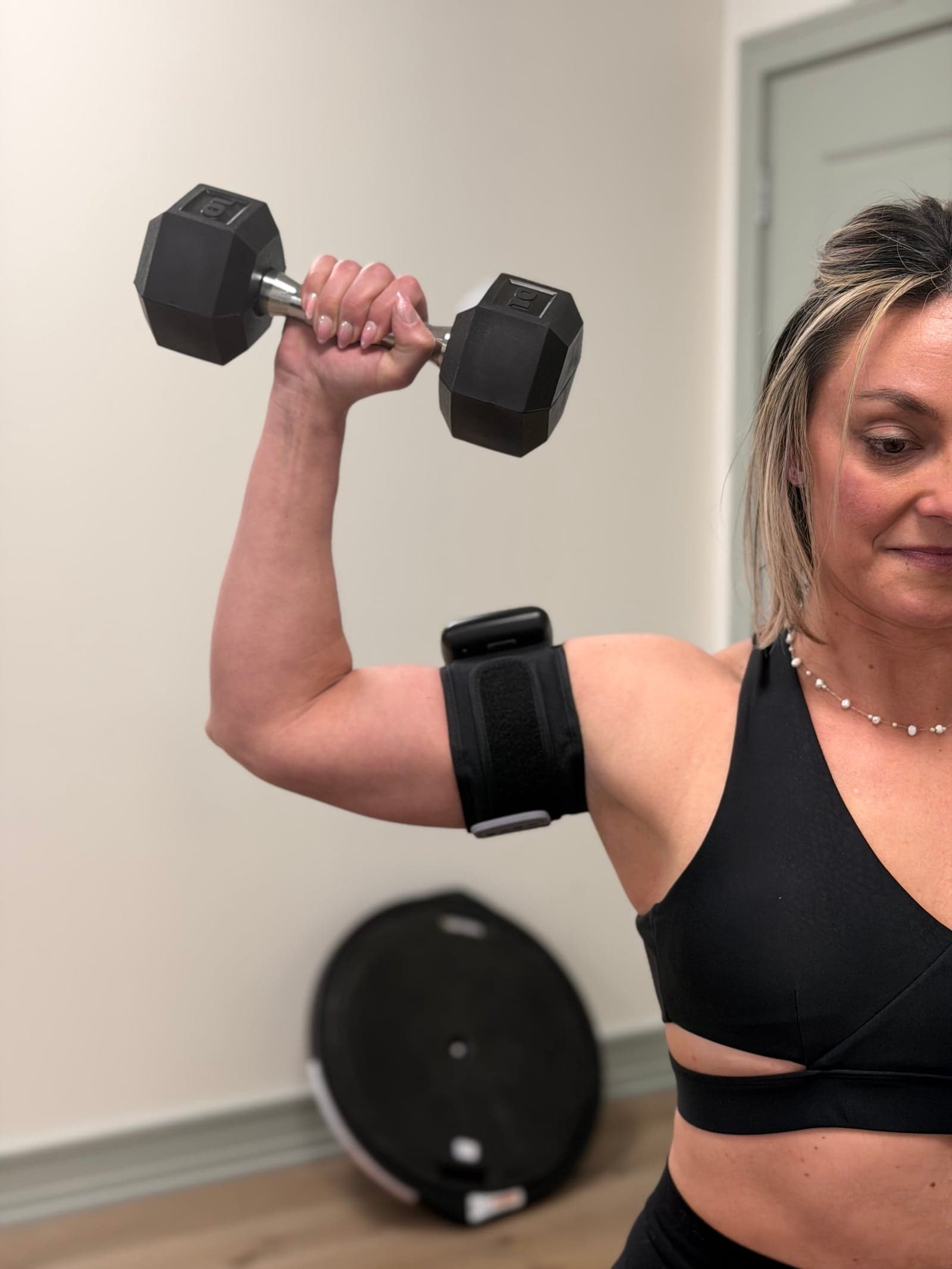Patient holding a dumbbell overhead with a SAGA BFR cuff on the upper arm during a one-on-one session at Thera Performance Lab in Lake Orion, Michigan